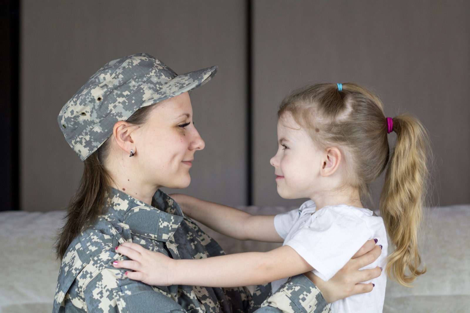 A service member in uniform at home, face to face with her young daughter