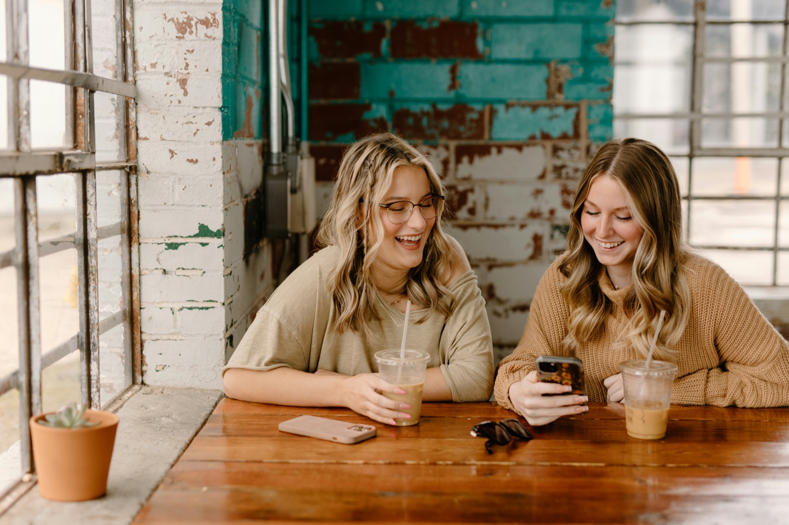 Two friends laughing together over a phone at a coffee shop