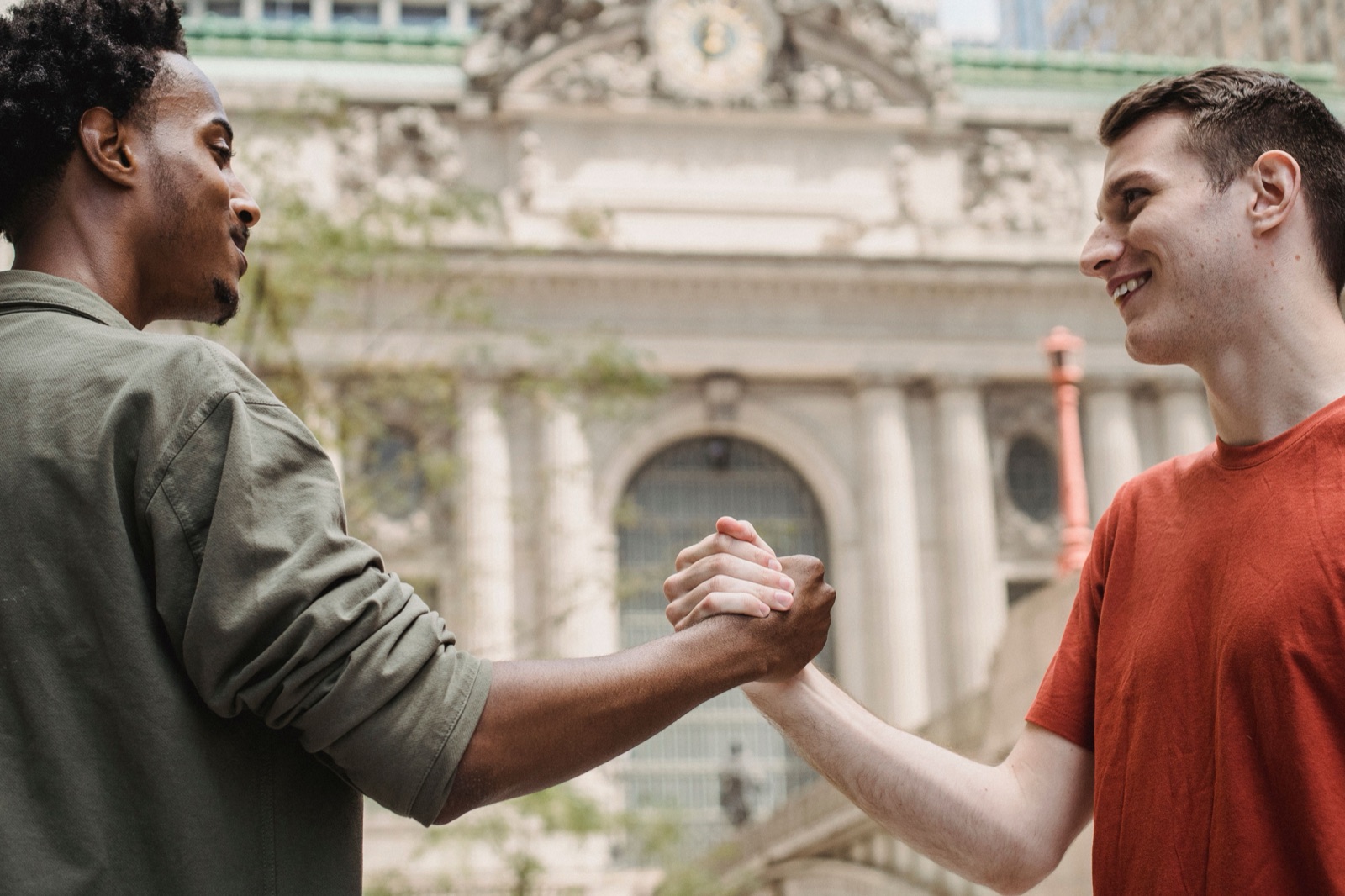 Two friends clasping hands in congratulations outside a campus building