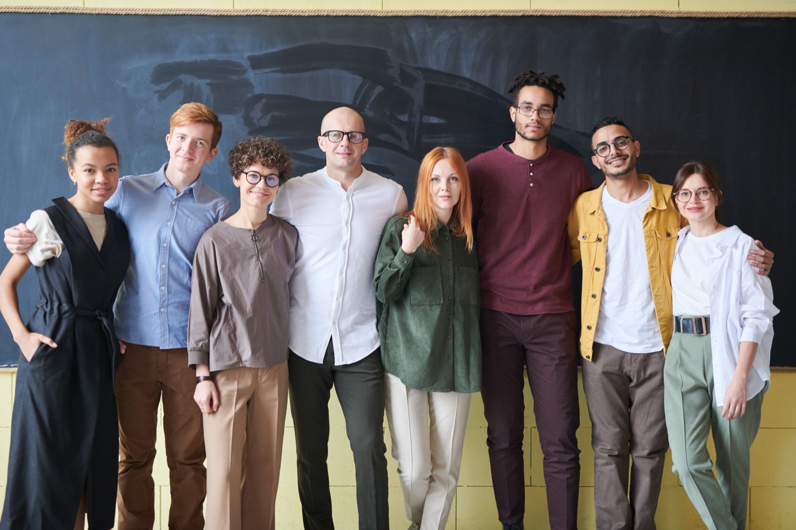 A cohort of classmates standing shoulder to shoulder in front of a chalkboard