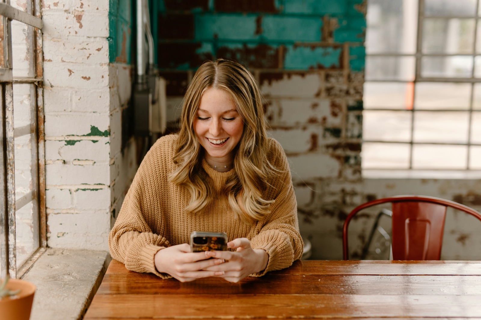 A woman at a cafe table smiling at an encouraging message on her phone