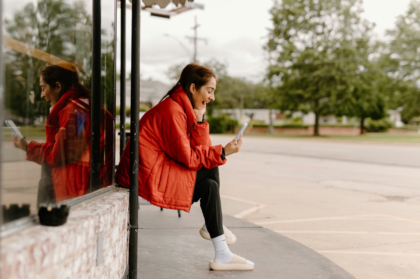 A woman sitting outside in a new neighborhood, smiling at a message from a friend